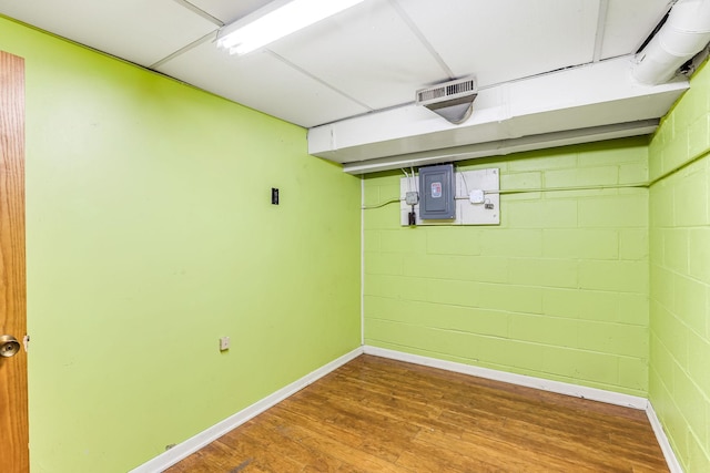 finished basement with wood finished floors, visible vents, baseboards, electric panel, and concrete block wall