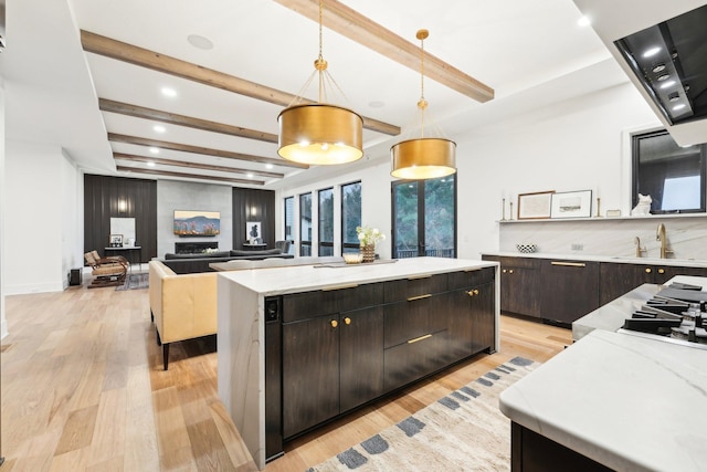 kitchen with light wood finished floors, a kitchen island, beam ceiling, a sink, and dark brown cabinets