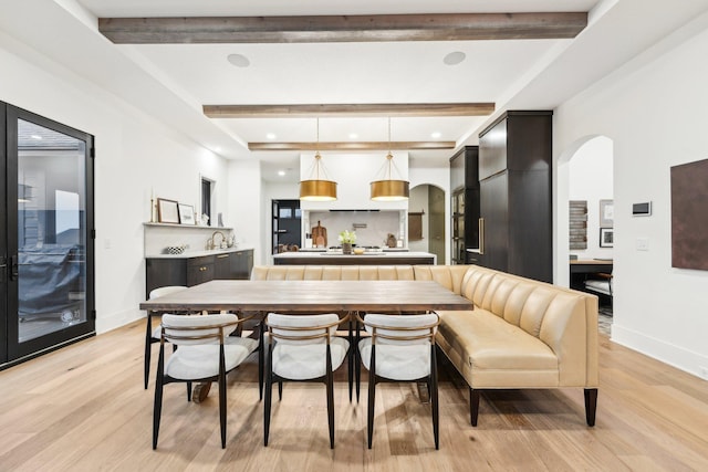 kitchen featuring arched walkways, beam ceiling, light wood-style flooring, and hanging light fixtures