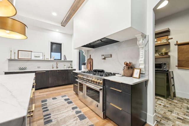 kitchen with light stone counters, range with two ovens, a sink, beamed ceiling, and light wood-type flooring