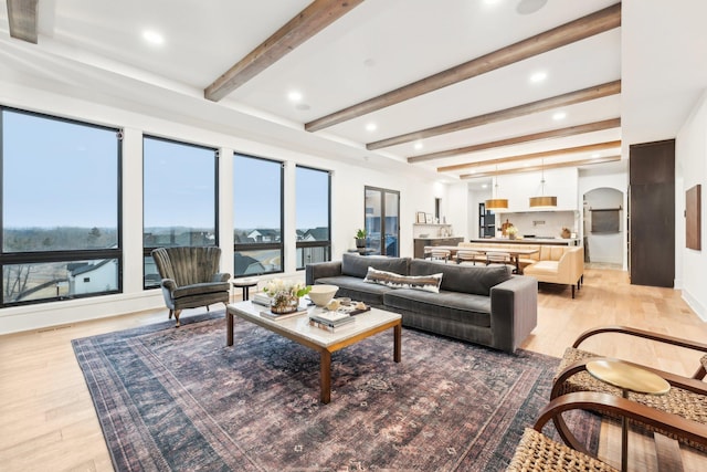 living area with beamed ceiling, recessed lighting, light wood-style floors, and arched walkways