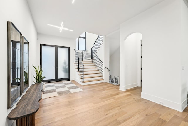 entrance foyer featuring stairway, french doors, arched walkways, and light wood finished floors