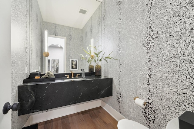 half bath with visible vents, baseboards, toilet, wood finished floors, and vanity