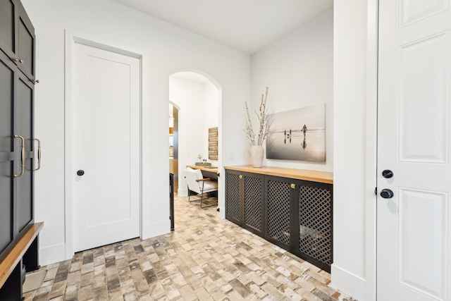 hallway featuring brick floor, baseboards, and arched walkways