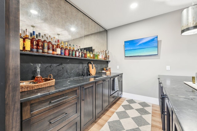 bar featuring baseboards, a sink, indoor wet bar, tasteful backsplash, and light wood-type flooring