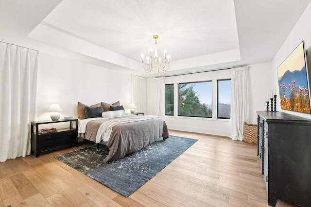 bedroom featuring a raised ceiling, a notable chandelier, baseboards, and light wood-type flooring