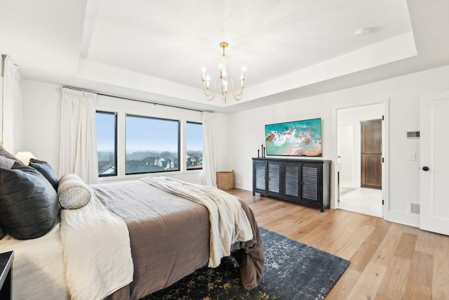 bedroom featuring a tray ceiling, baseboards, an inviting chandelier, and light wood finished floors