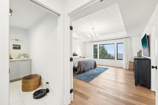 bedroom with a tray ceiling, baseboards, a notable chandelier, and light wood finished floors