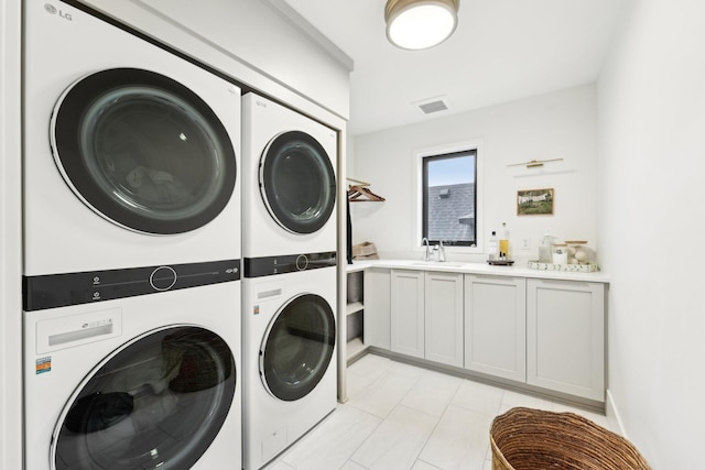 laundry area featuring visible vents, cabinet space, a sink, stacked washer and clothes dryer, and washer and dryer