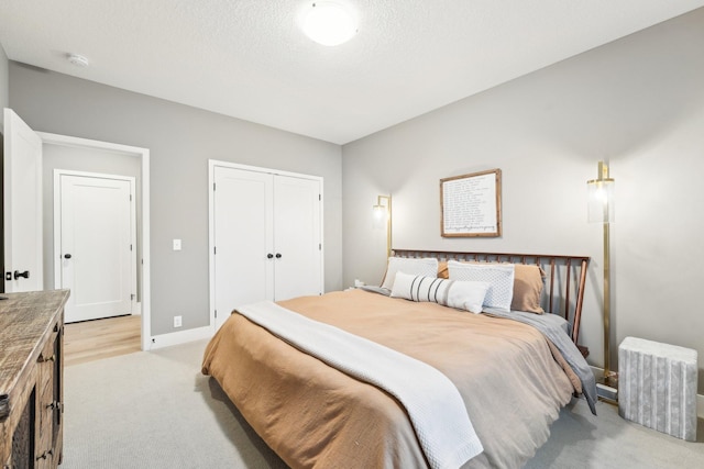 bedroom with a closet, light colored carpet, a textured ceiling, and baseboards