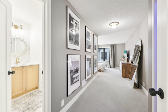 hallway with a sink, a textured ceiling, baseboards, and carpet floors