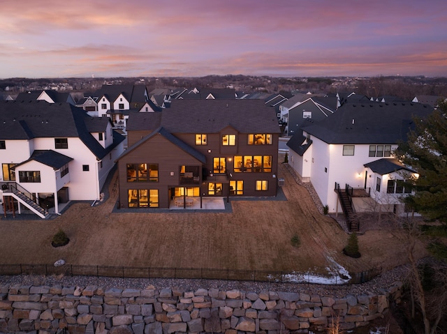 back of property at dusk featuring fence, a residential view, and driveway