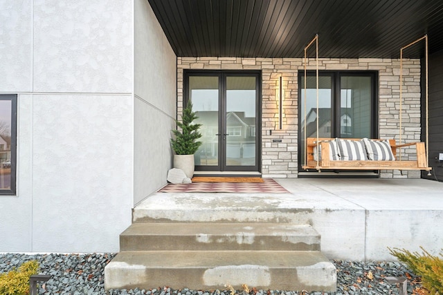 entrance to property with a porch, stone siding, and stucco siding