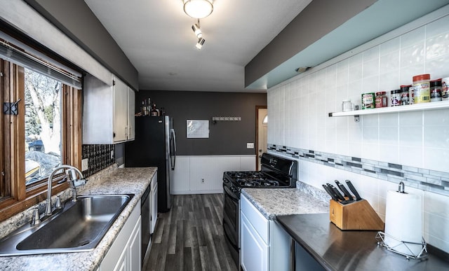 kitchen with dark wood finished floors, wainscoting, black gas range oven, a sink, and backsplash