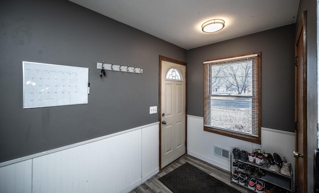 doorway to outside with mail area, visible vents, wood finished floors, and wainscoting