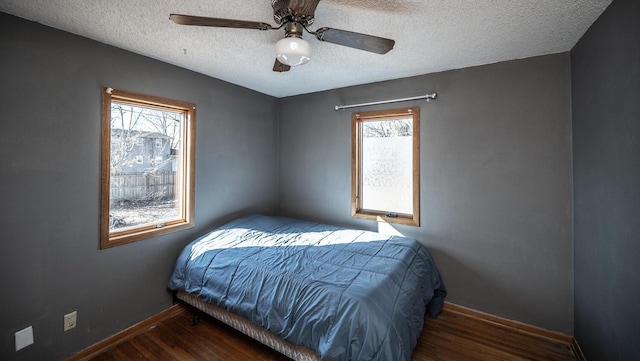 bedroom with a textured ceiling, multiple windows, wood finished floors, and baseboards