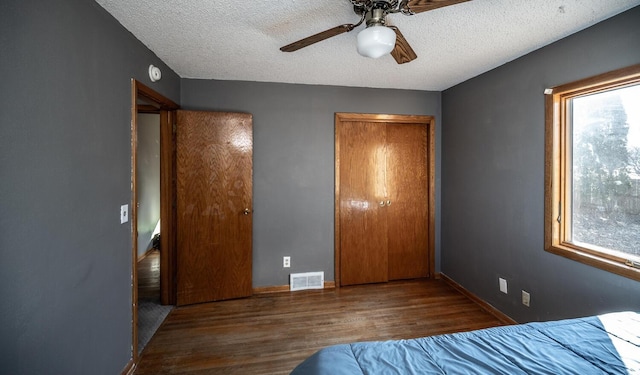 unfurnished bedroom with a textured ceiling, multiple windows, wood finished floors, and visible vents