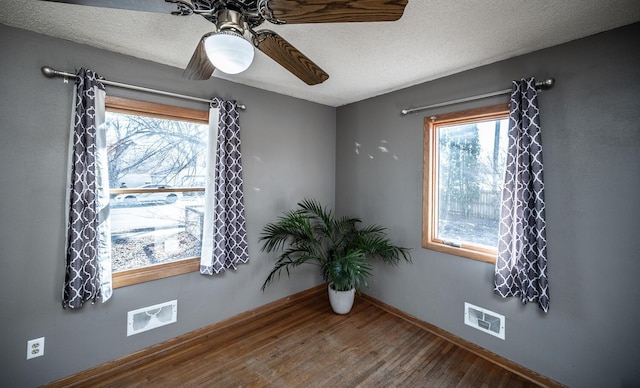 empty room with a textured ceiling, ceiling fan, wood finished floors, and visible vents