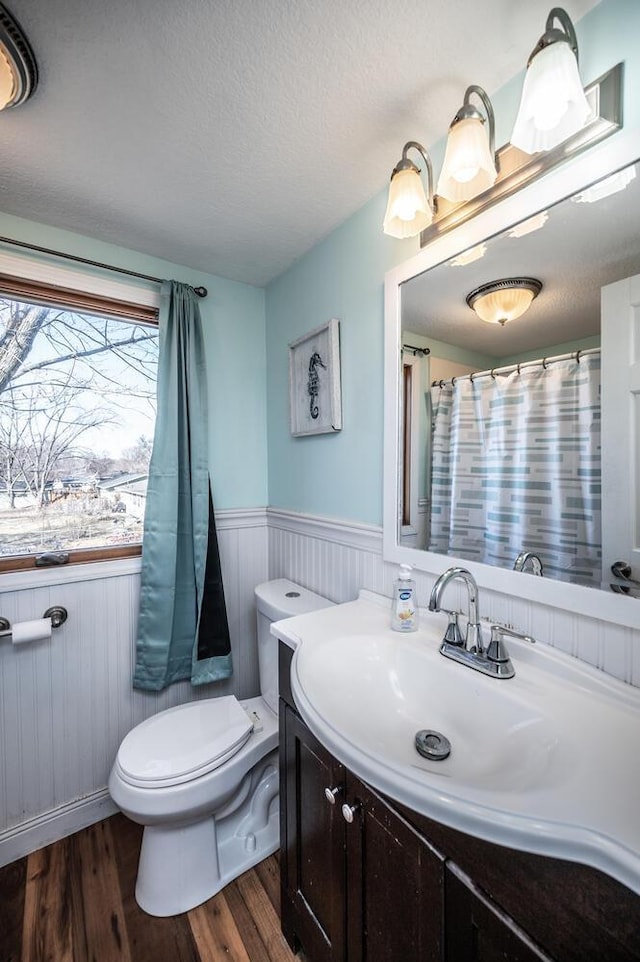 bathroom featuring toilet, a wainscoted wall, wood finished floors, a textured ceiling, and vanity