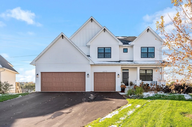 modern inspired farmhouse with metal roof, a porch, aphalt driveway, a front lawn, and board and batten siding