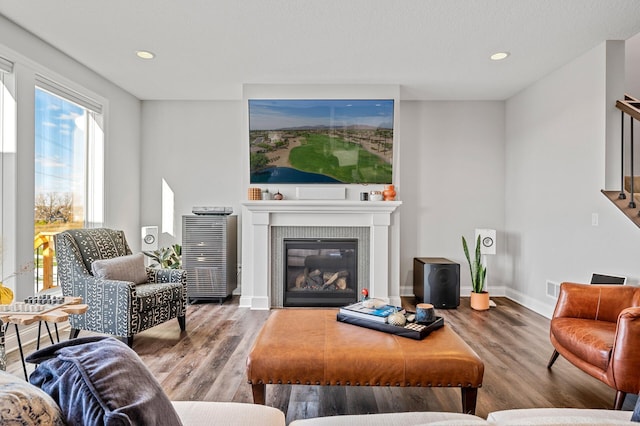 living area featuring a glass covered fireplace, recessed lighting, wood finished floors, and baseboards