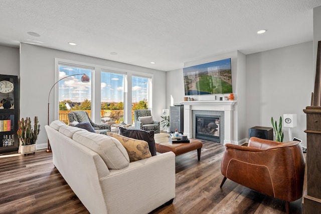 living room with dark wood-style floors, a glass covered fireplace, and a textured ceiling