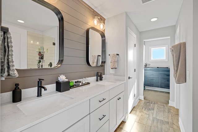 full bath with double vanity, a sink, and wooden walls