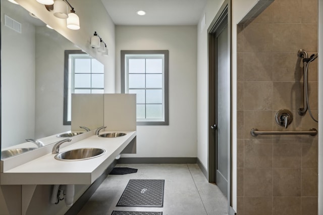 bathroom with tiled shower, double sink, visible vents, and baseboards