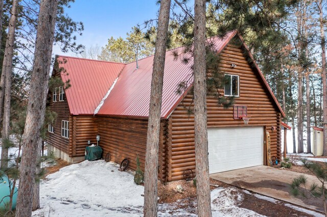 snow covered property with metal roof, log exterior, driveway, and a garage