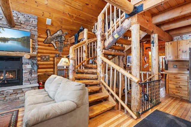 stairway with a stone fireplace, wooden ceiling, hardwood / wood-style flooring, beam ceiling, and rustic walls