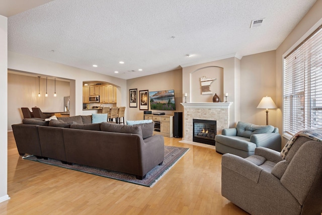 living room with visible vents, a tile fireplace, light wood-style flooring, a textured ceiling, and recessed lighting