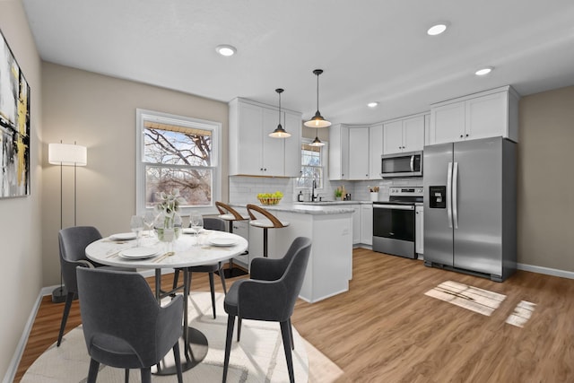 kitchen with stainless steel appliances, white cabinetry, light wood-style floors, backsplash, and pendant lighting