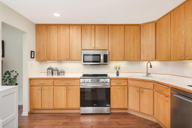 kitchen with light countertops, stainless steel appliances, decorative backsplash, and a sink