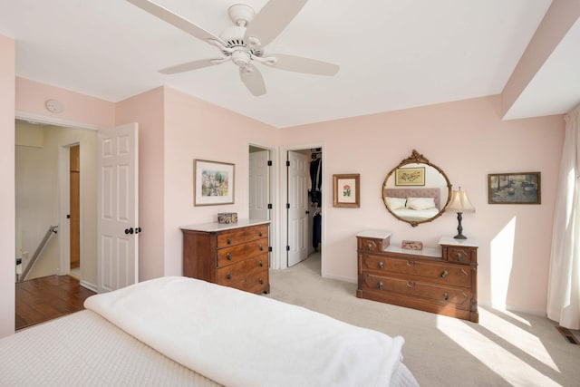 bedroom featuring a closet, baseboards, ceiling fan, light colored carpet, and a spacious closet