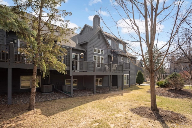 back of property with a chimney, central air condition unit, a wooden deck, and a lawn