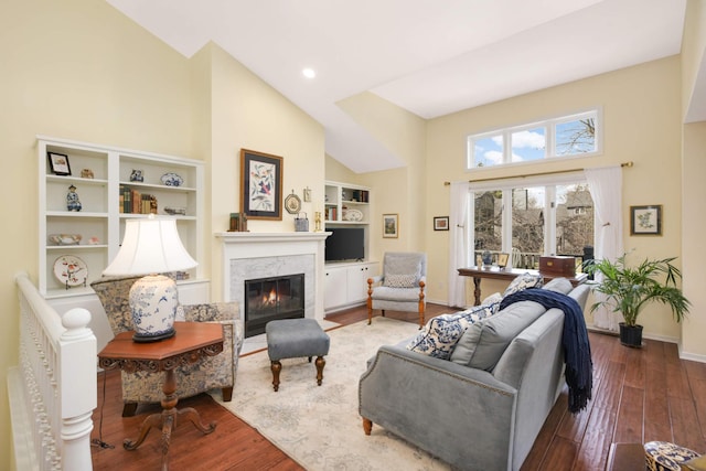 living room with baseboards, a glass covered fireplace, wood-type flooring, built in shelves, and high vaulted ceiling