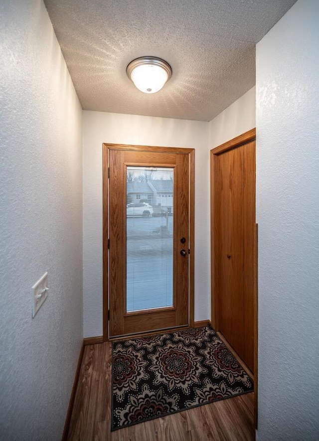 entryway featuring a textured wall, a textured ceiling, baseboards, and wood finished floors