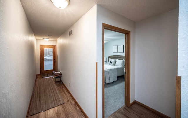 corridor with visible vents, a textured ceiling, baseboards, and wood finished floors