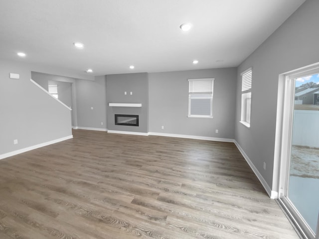 unfurnished living room with recessed lighting, baseboards, wood finished floors, and a glass covered fireplace