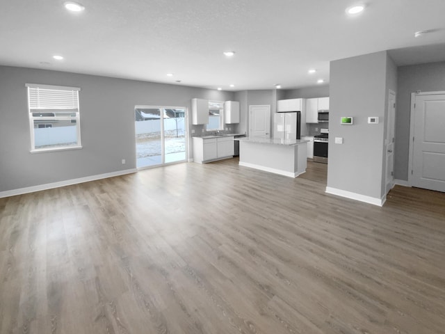 unfurnished living room featuring recessed lighting, a sink, baseboards, and wood finished floors