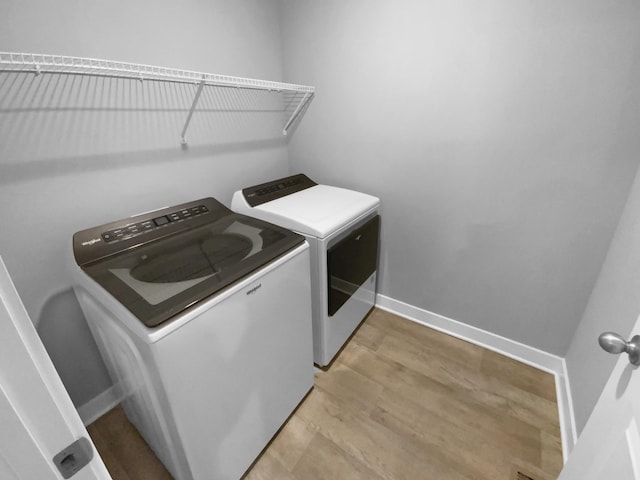 washroom featuring washing machine and dryer, laundry area, light wood-style flooring, and baseboards