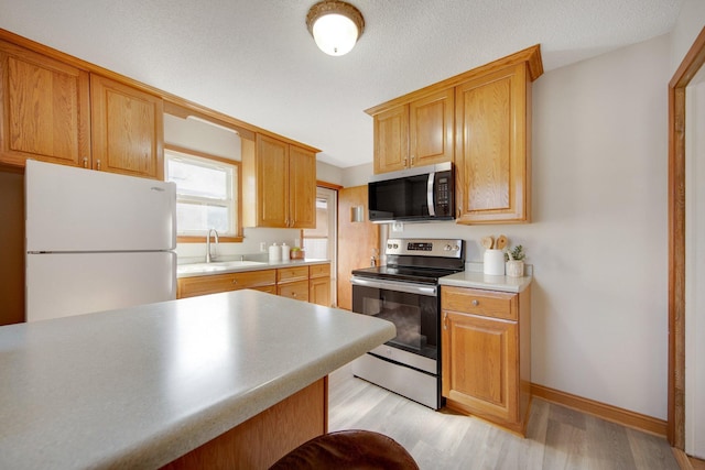 kitchen with a sink, baseboards, light wood-style floors, light countertops, and appliances with stainless steel finishes