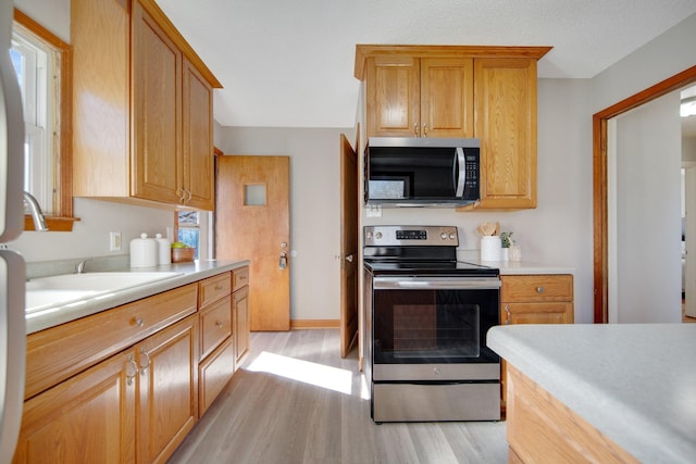 kitchen featuring baseboards, appliances with stainless steel finishes, light countertops, light wood-type flooring, and a sink