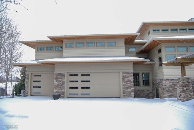 prairie-style home with a garage, stone siding, and fence