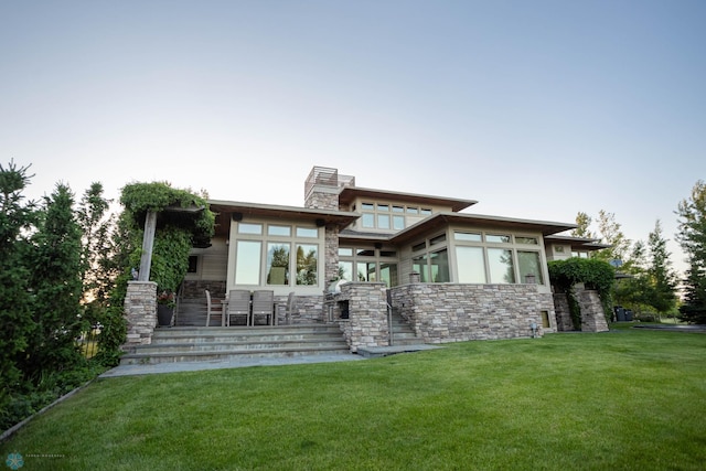 back of property featuring stone siding, a lawn, and a chimney