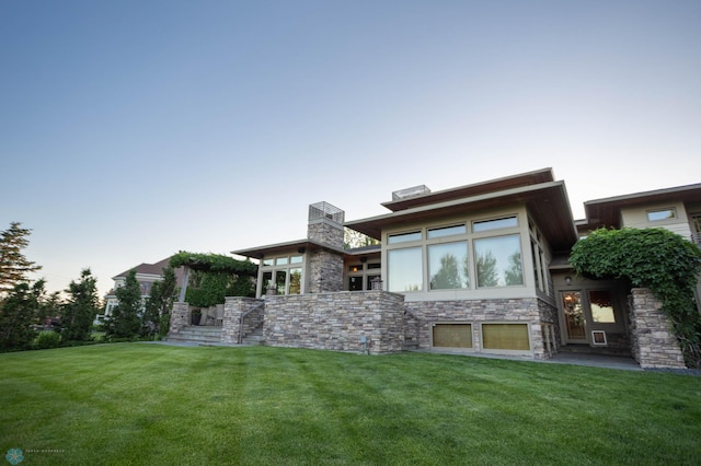 rear view of house featuring an attached garage, stone siding, and a yard