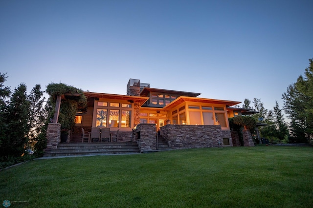 rear view of property featuring stone siding, a chimney, a sunroom, and a lawn