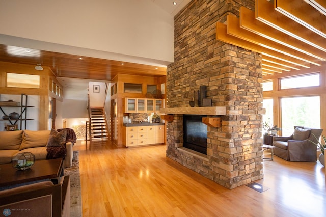 living room with a stone fireplace, light wood finished floors, stairway, and a high ceiling