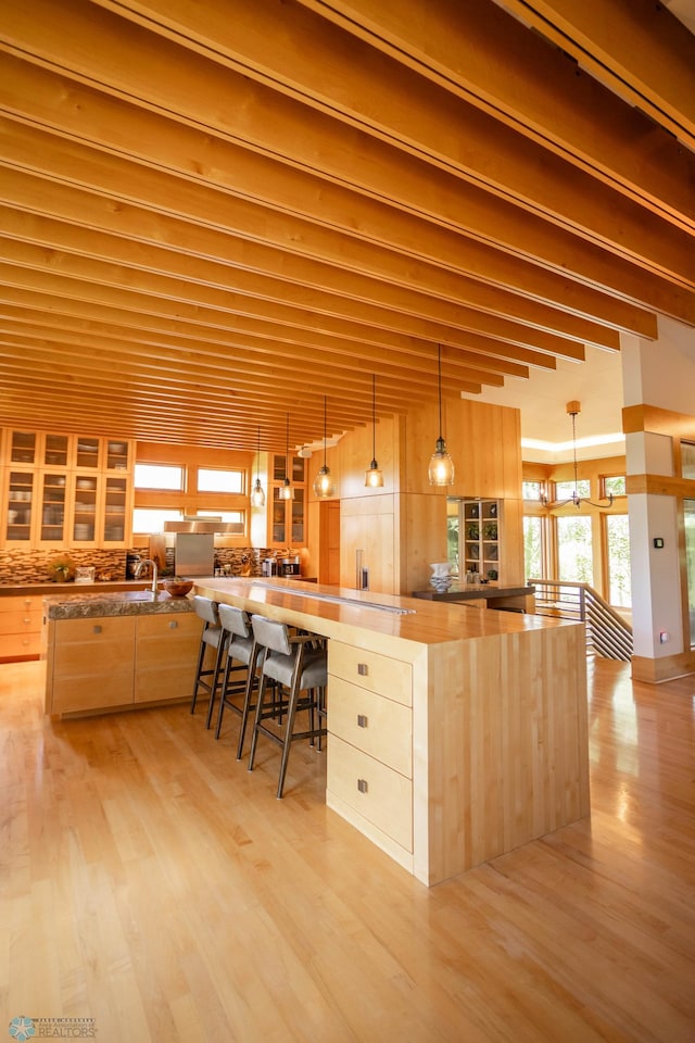 kitchen with pendant lighting, a notable chandelier, light brown cabinets, light wood-type flooring, and beamed ceiling