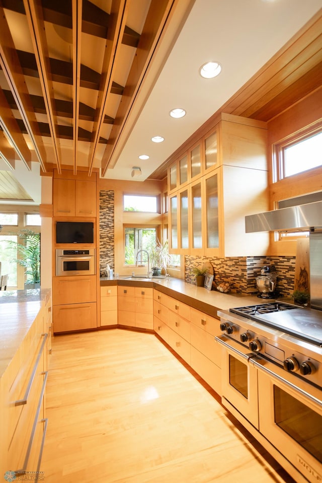 kitchen with a sink, stainless steel appliances, light wood-type flooring, light brown cabinets, and backsplash